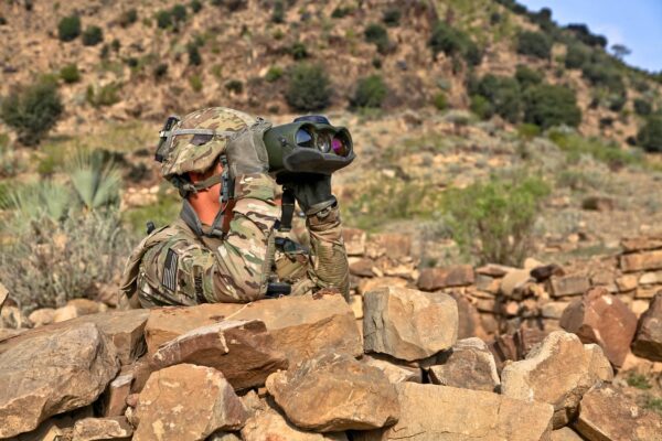 Pentagon military soldier scouting with binoculars in desert terrain, on ground operations