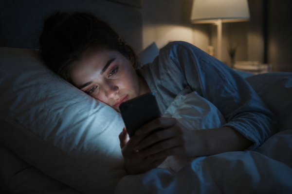 Woman lying in bed using smartphone late at night, illustrating digital addiction and sleep disruption – bdesk.news